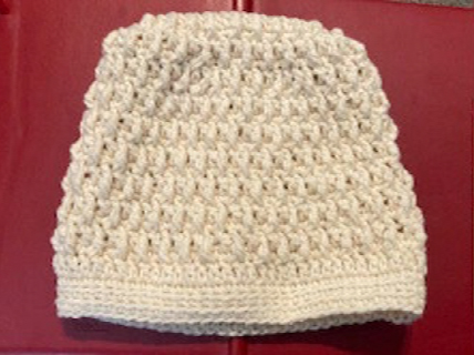 A white crocheted beanie on a red surface.